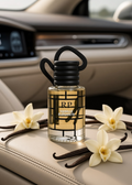 A clear glass perfume bottle with a black ribbed cap and black hanging cord, labeled RP Vanie Elegante, placed on a beige leather car seat with vanilla beans and white flowers around it.