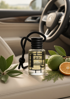 A clear glass car fragrance bottle labeled RP BALE QALDER with a black cap and hanging cord, styled on a beige car seat with green leaves, a lime, and an orange slice nearby. The blurred car interior and steering wheel are in the background.
