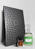 A gift set featuring a large dark gray patterned box with a central 'RP Paris' logo, a small clear bottle with an orange label and black cap, and a clear spray bottle with a green label reading 'BAIE D'ALGER'.