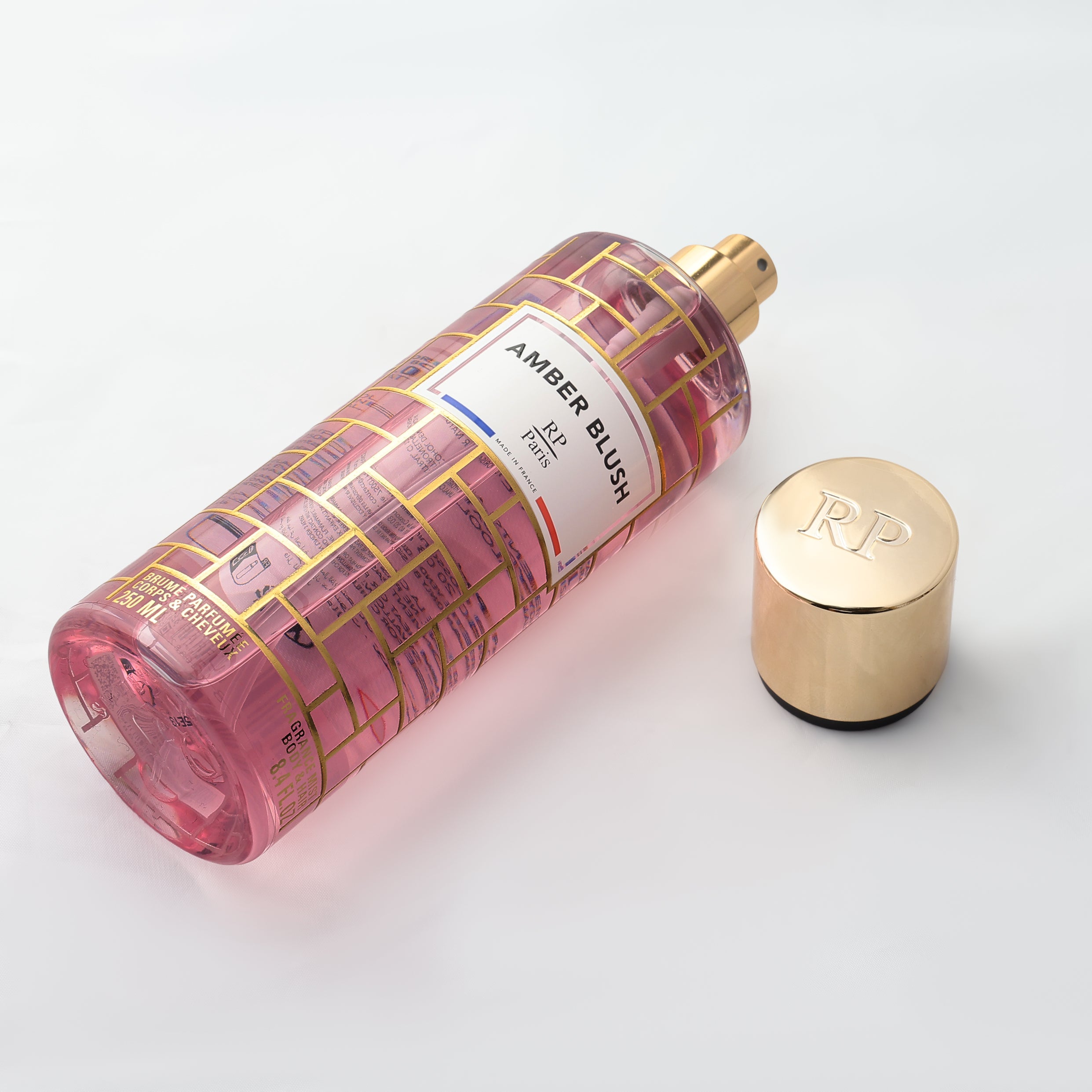 Angled view of the Amber Blush by RP Paris perfume bottle with gold cap and amber fragrance on a light gray background.
