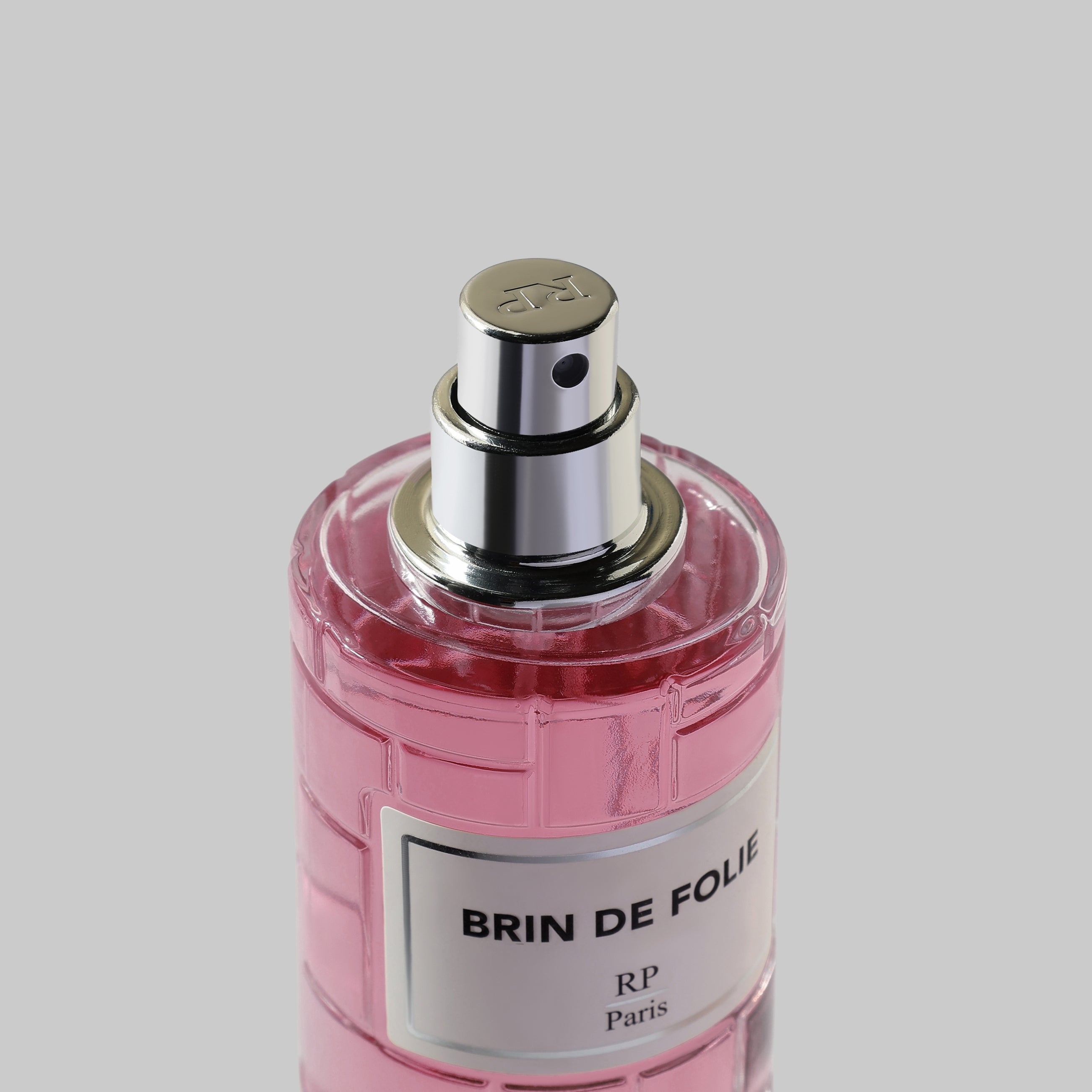 Perfume bottle labeled 'BRIN DE FOLIE' with pink liquid on a gray background