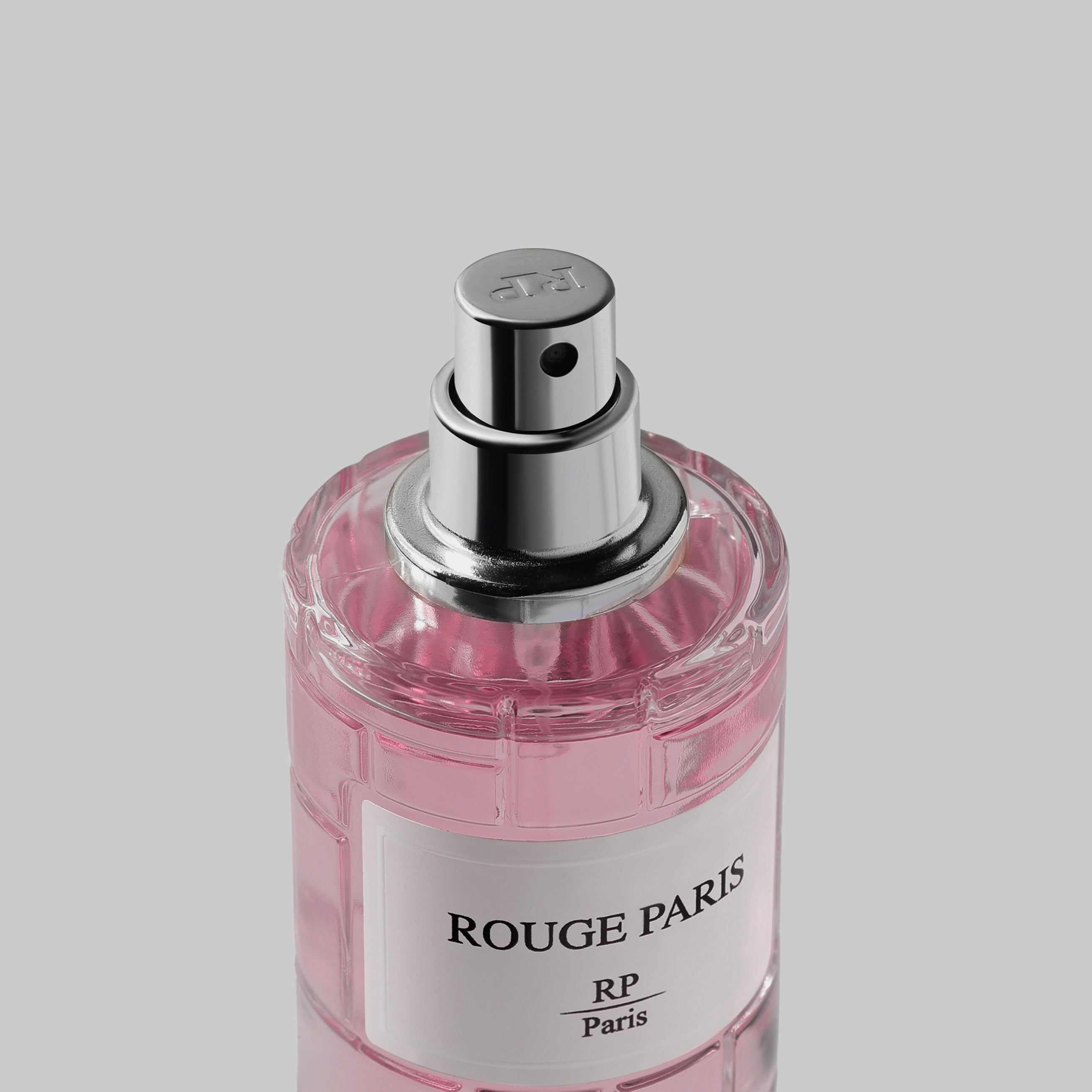 Pink perfume bottle with silver cap labeled 'Rouge Paris' on a light gray background