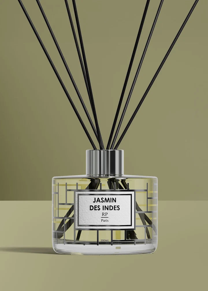 A reed diffuser bottle with black reeds, a clear glass body, and a white label reading 'JASMIN DES INDES R.F.