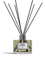 A reed diffuser bottle with a clear glass body, pale yellow liquid, a white label reading 'ROSE DE MAI BP Paris,' and multiple black reed sticks extending upward against a white background.