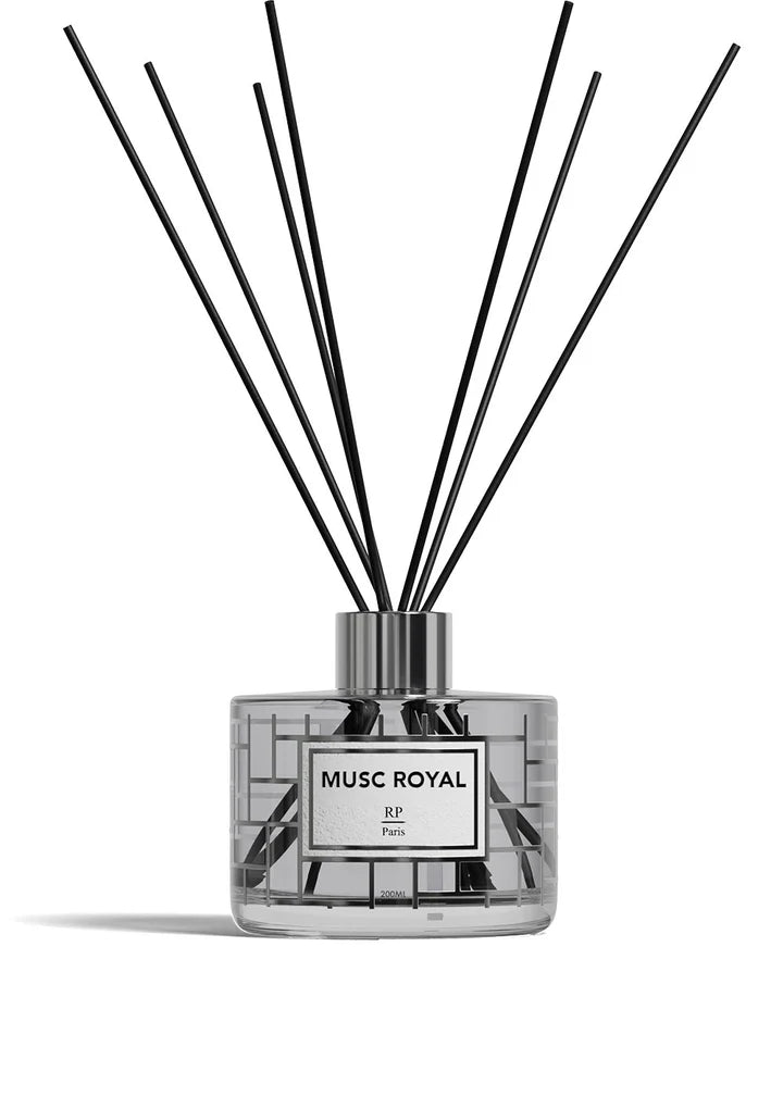 A reed diffuser bottle with a clear glass body, pale yellow liquid, a white label reading 'ROSE DE MAI BP Paris,' and multiple black reed sticks extending upward against a white background.