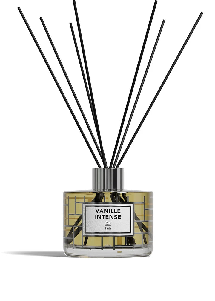 A reed diffuser bottle with a clear glass body, yellow liquid, a white label reading 'VANILLE INTENSE BP Paris,' and multiple black reed sticks extending upward on a white background.