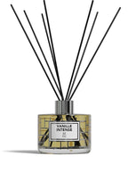 A reed diffuser bottle with a clear glass body, yellow liquid, a white label reading 'VANILLE INTENSE BP Paris,' and multiple black reed sticks extending upward on a white background.