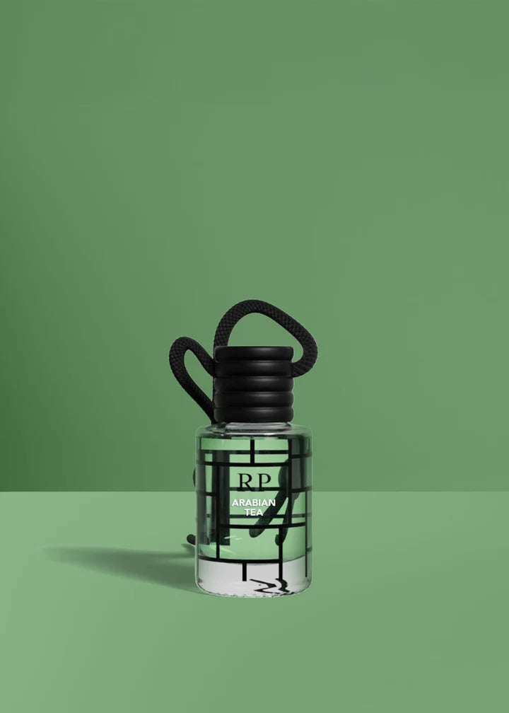 A small clear bottle with a black cap and black hanging loop, filled with a pale green liquid, set against a solid green background. The bottle has a black geometric line pattern and a visible RP logo.