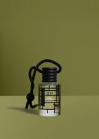 A clear glass bottle of RP by Rude Paris diffuser with a black cap and black hanging cord, set against a solid olive green background.