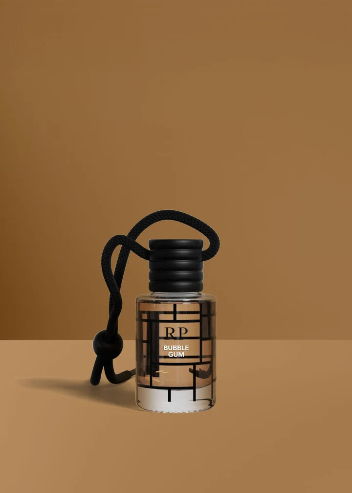 A clear cylindrical bottle of RP Bubble Gum fragrance with a black cap and black hanging cord, set against a warm brown studio background.