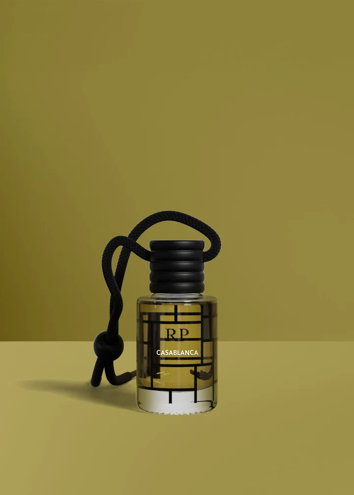 A small clear glass bottle with a black ribbed cap and black hanging cord, labeled RP Casablanca, set against a solid olive-green background.