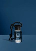 A small clear glass bottle with a black screw cap and black hanging cord, labeled RP oud mood, set against a dark blue studio background.