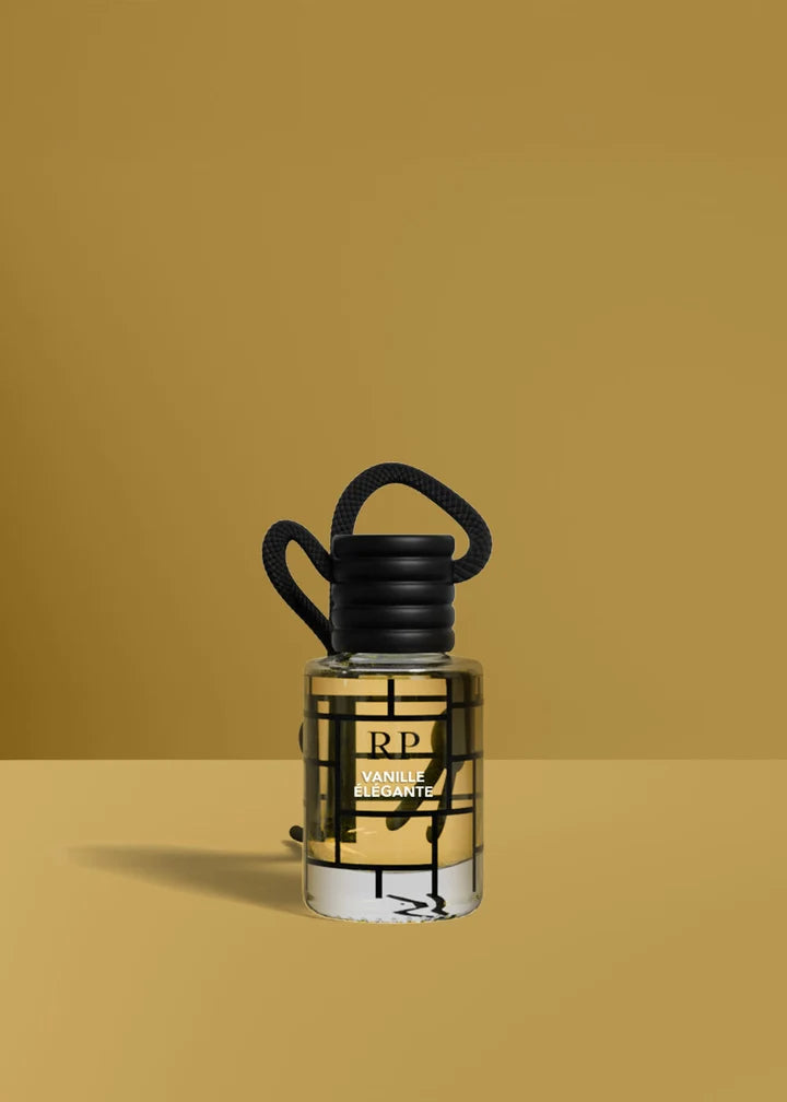 A small clear glass bottle of RP Rarely Seen Fragrance with a black cap and black hanging loop, filled with amber liquid, set against a solid mustard yellow background.