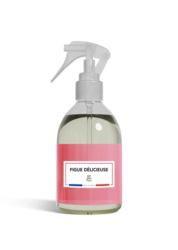 A clear plastic spray bottle filled with a pale yellow liquid, featuring a translucent white spray nozzle and a pink label with the text 'FIGUE DÉLICIEUSE' and 'BF Paris'.