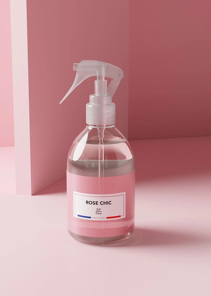 A clear spray bottle filled with pink liquid, featuring a white trigger sprayer and a white label that reads 'ROSE CHIC' with 'SP Paris' underneath, set against a minimalist pink background.