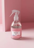 A clear spray bottle filled with pink liquid, featuring a white trigger sprayer and a white label that reads 'ROSE CHIC' with 'SP Paris' underneath, set against a minimalist pink background.