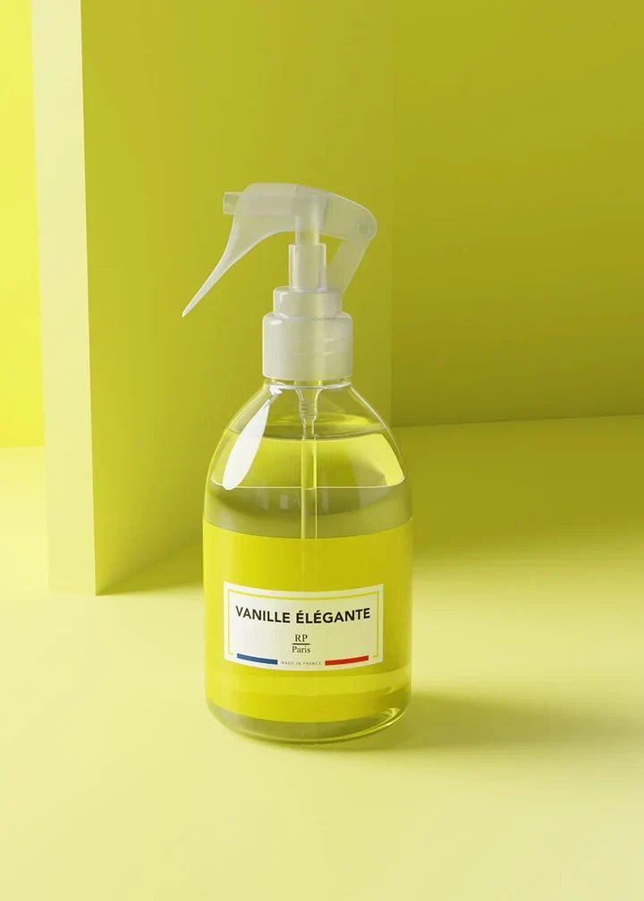A clear spray bottle filled with pale yellow liquid, featuring a white trigger sprayer and a white label that reads 'VANILLE ÉLÉGANTE' with '24h Paris' below. The bottle is set against a minimalist lime green background.