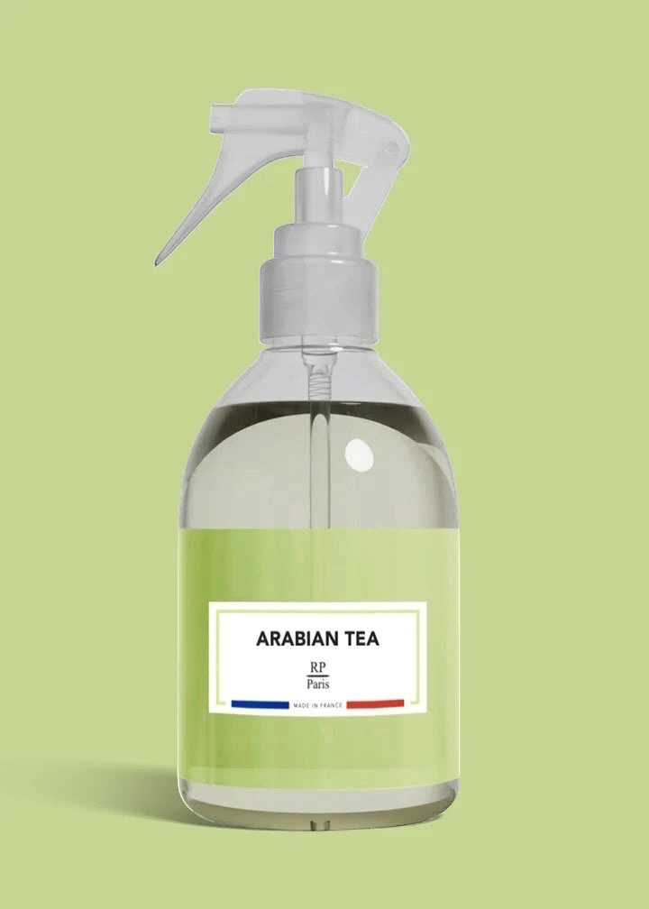 A clear plastic spray bottle filled with a pale green liquid, featuring a white trigger sprayer and a white label that reads 'ARABIAN TEA' with '3-3 Paris' and small blue and red accents, set against a solid light green background.
