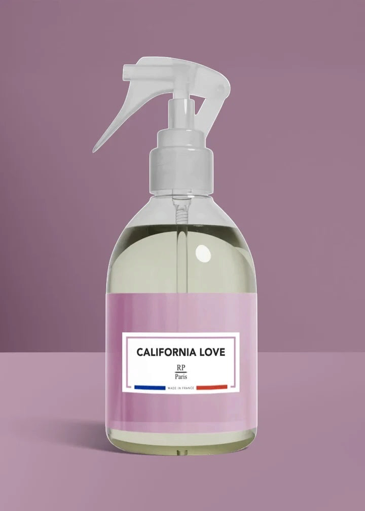 A clear plastic spray bottle with a white trigger sprayer and a pink label reading 'CALIFORNIA LOVE' and 'BP Paris', set against a solid mauve background.