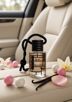 A small bottle of bubble gum fragrance with a black cord loop sits on a beige car seat, surrounded by pink and white gum balls, vanilla beans, and flower petals.