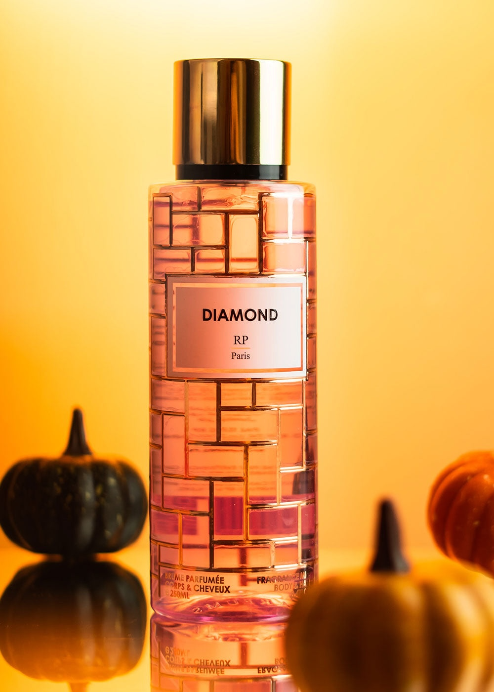 Diamond perfume bottle with pumpkins on a reflective surface against a yellow background